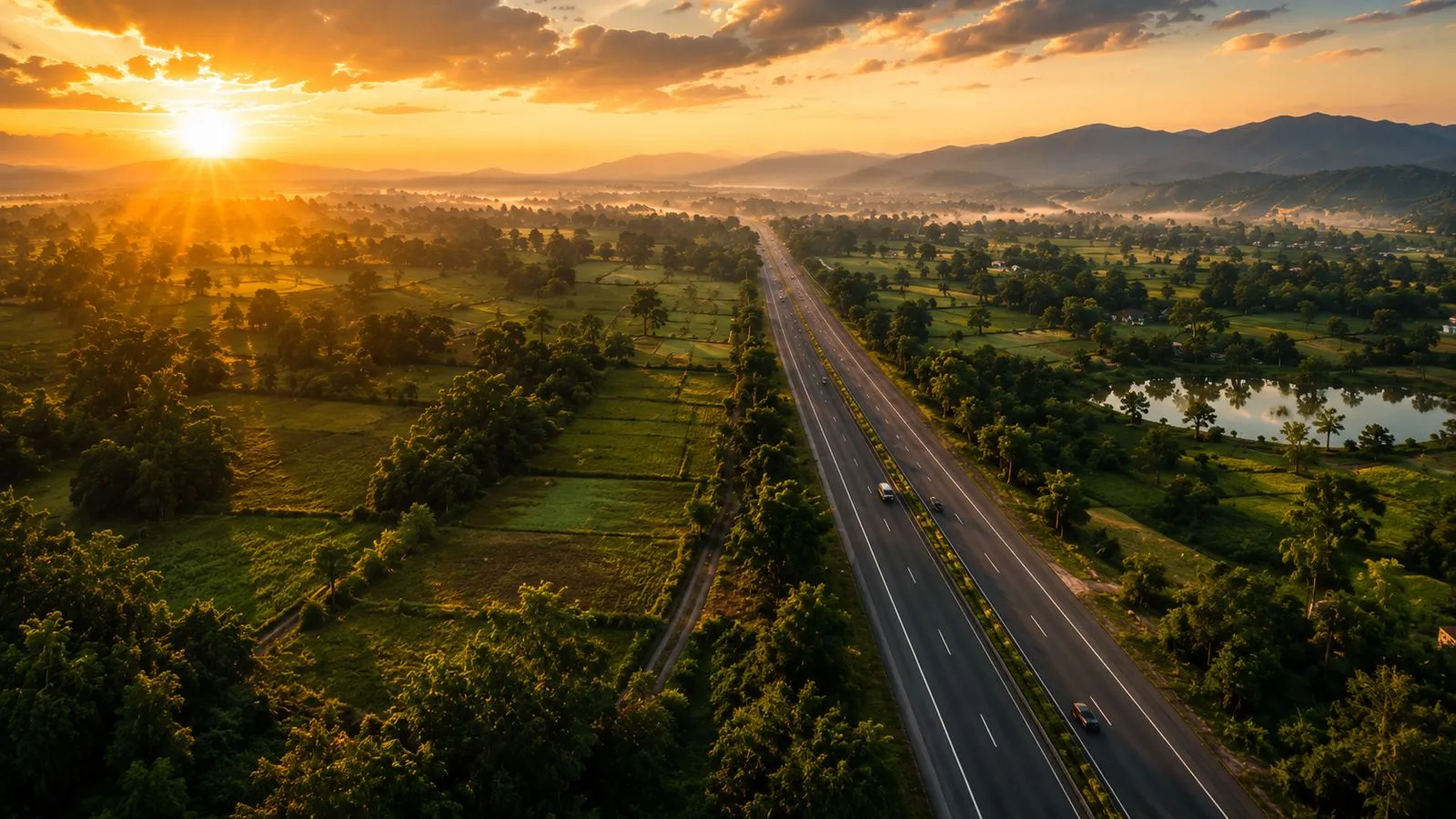 Aerial golden-hour view of the NH731 highway winding through lush green farmland valleys with misty mountains